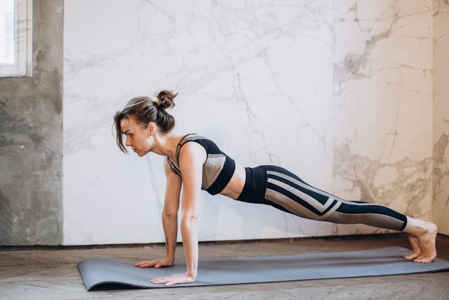 Femme en tenue de sport noire et grisesur un tapis de yoga gris qui fait du gainage