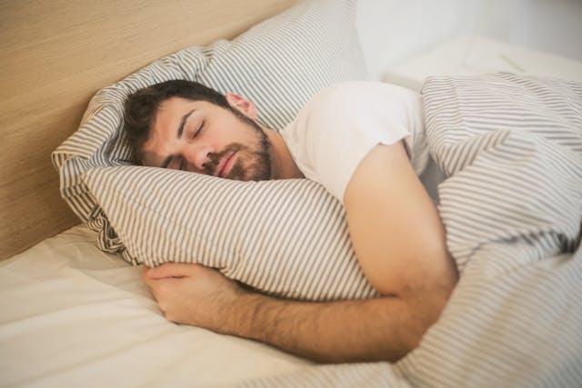 Homme brun avec tee-shirt blanc qui dort sur le côté avec couette et taie d'oreiller à rayures beiges et blanches